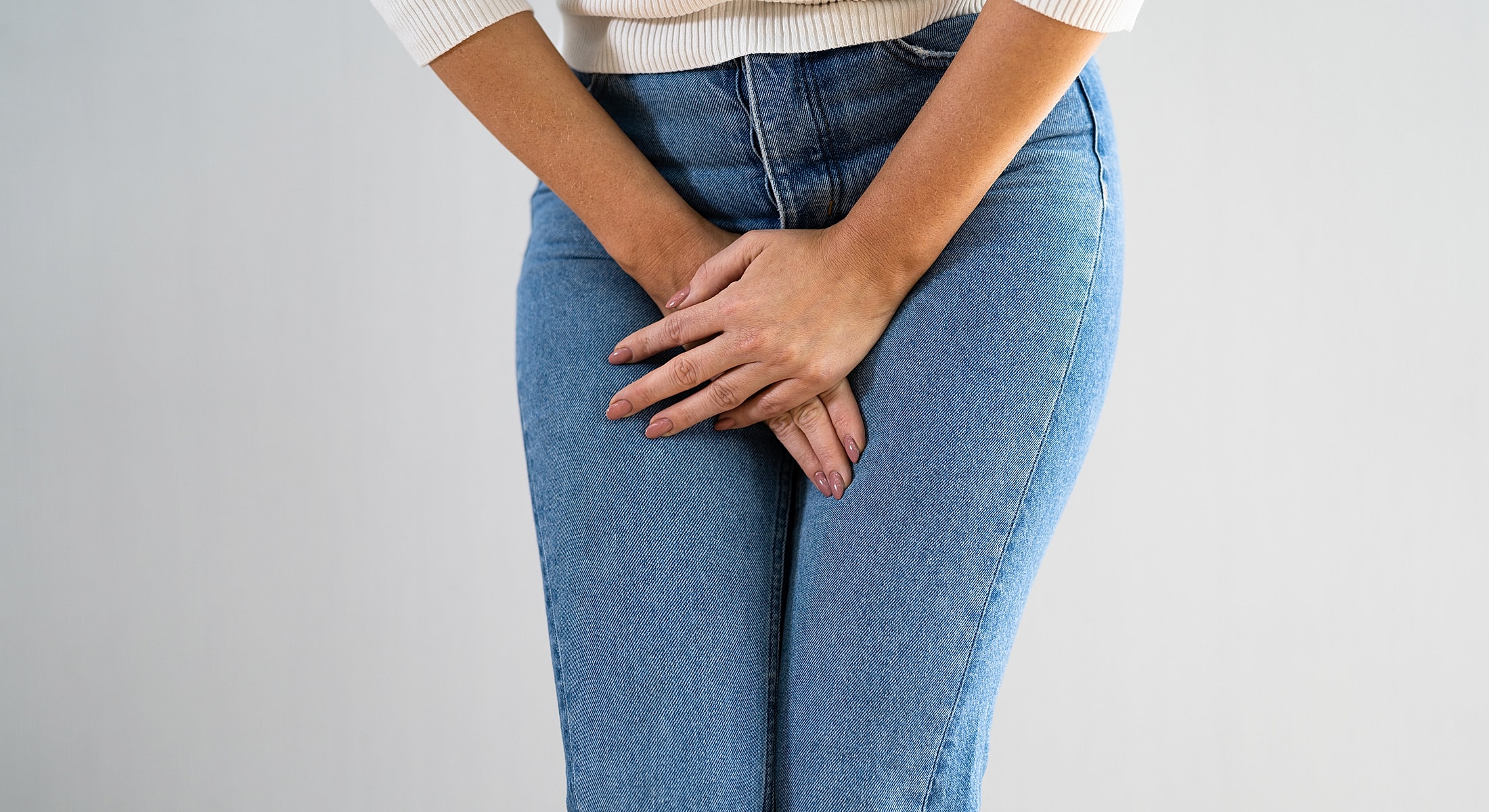 Woman holding hands over her lap in jeans.